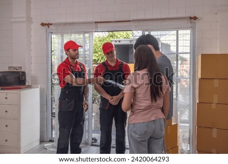 A homeowner signs documents to approve the moving job while professional movers in red uniforms await confirmation.