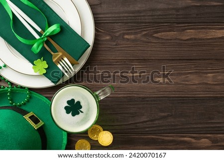 Toast to St. Patrick's in style: top view of plate, napkin-wrapped utensils, glass of beer, leprechaun's hat, gold coins, trefoils, beads on wooden desk canvas. Perfect for your festive announcements