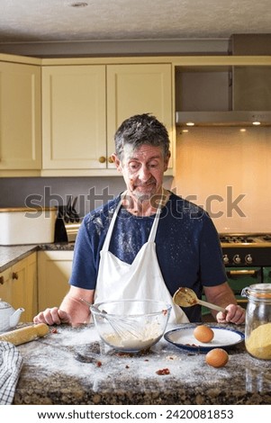Cookery lessons. A humorous picture of a attempting to cook as he pulls a confused and defeated face. Kitchen image of food preparation and cooking.