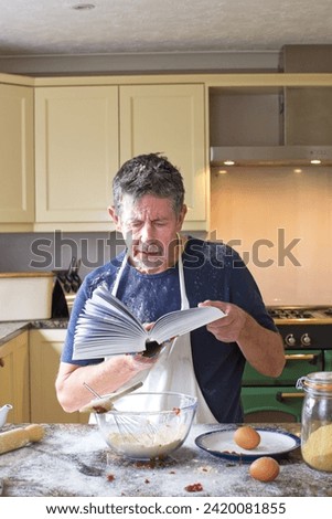 Cookery lessons. A humorous picture of a man reading a cookery book with a confused look on his face as attempts to cook or prepare food.