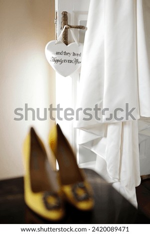 A heart-shaped sign hanging on the vintage door handle with the inscription 'and they lived happily ever after,' alongside a bridal gown detail hung on the door. stock photo