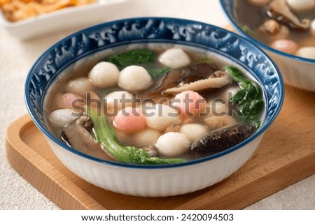 Eating red and white small tangyuan, tang yuan, glutinous rice dumpling balls with savory soup in a bowl on white table background. Royalty-Free Stock Photo #2420094503