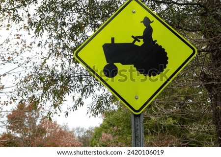 Fluorescent green triangular yield sign with the silhouette of a farmer on a tractor with trees in the background