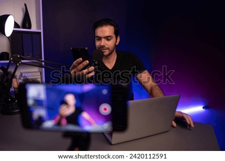 Broadcaster talking to listener on live streaming online with blurred screen, reading comment on smartphone on social media channel by creative positive thinking at purple neon light studio. Surmise.