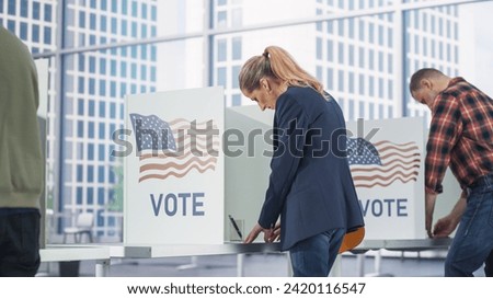 Businesswoman Filling Out a Ballot in a Voting Booth on the Day of National Elections in the United States. Adult Men and Women Voting for Elected Officials in a Polling Place. View from the Back Royalty-Free Stock Photo #2420116547