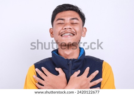 Calm young Asian man with dental braces closed eyes and holding his chest feeling relieved and happy Royalty-Free Stock Photo #2420122677