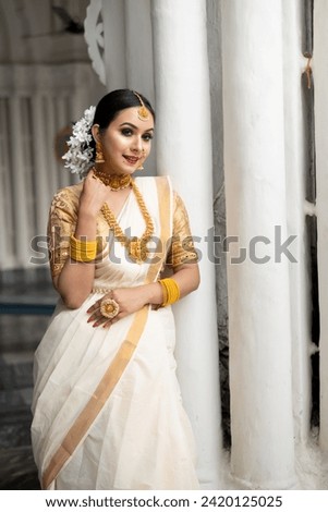 Stunning bride dressed in a traditional Indian bridal saree with gold jewellery smiles tenderly in front of a vintage background. Wedding fashion and lifestyle. Royalty-Free Stock Photo #2420125025