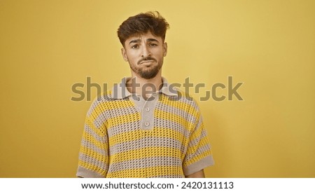 Stylish young arab man coolly bears his serious expression, standing lone against a stark yellow background. Royalty-Free Stock Photo #2420131113