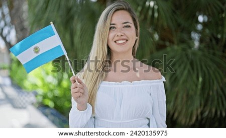 Young blonde woman smiling confident holding argentina flag at park