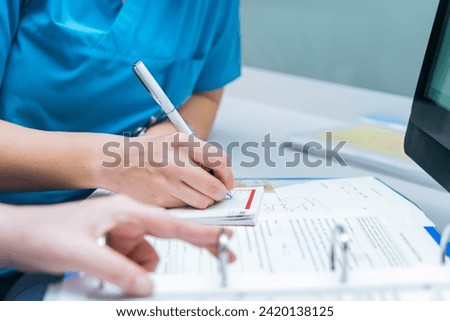 two nurses share patient information by writing it on the patient file, sharing paperwork and reviewing medical chart examination room. medical research or surgery planning in wellness hospital.