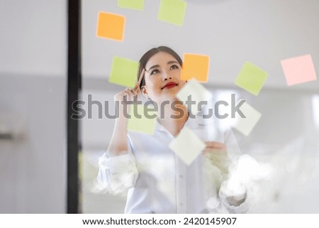 Happy asian businesswoman planning new project with sticky note in a creative writing on blank office glass
