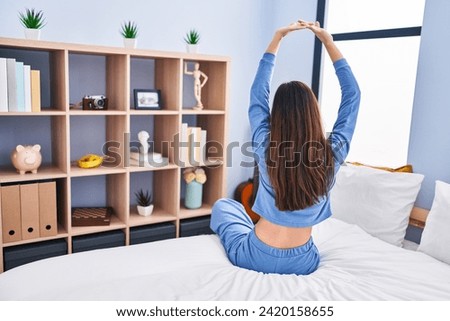 Young beautiful hispanic woman waking up stretching arms on back view at bedroom