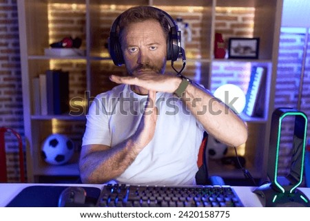 Middle age man with beard playing video games wearing headphones doing time out gesture with hands, frustrated and serious face  Royalty-Free Stock Photo #2420158775