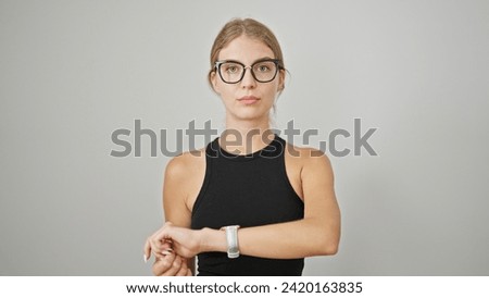 Young blonde woman standing with serious expression looking watch over isolated white background