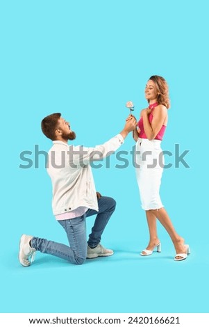 Young man giving rose to his girlfriend on blue background