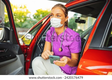 A female doctor reads text messages before while sitting in her car in a hospital parking lot. Young female doctor sitting in her car at parking and checking her phone.