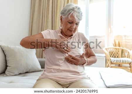 Elderly woman suffering from breast pain. Cropped close up of an unrecognizable woman experiencing cardiac discomfort at home. Close-up of a senior woman's hand on breast showing cancer symptom.