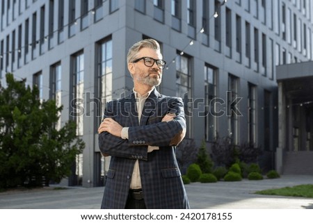 Mature, well-dressed senior businessman with a confident stance outside a modern office structure, exuding experience and professionalism.