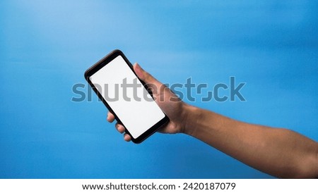 Hand of man holding mobile smartphone and showing blank phone screen on blue background
