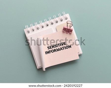Sensitive Information word on the paper and notepad with pink binding clip on pastel green background