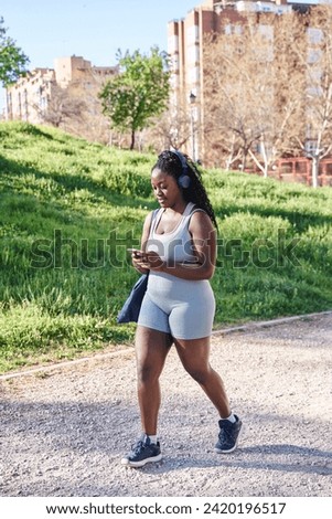 attractive curvy african american woman walking in sportswear while using her smartphone Royalty-Free Stock Photo #2420196517
