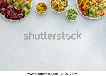 Preparing fresh vegetables in summer for winter, various frozen vegetables and berries in plates on a gray background, top view, copy space