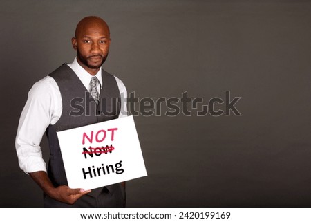 Young Black Business Man holding a not hiring sign with now hiring crossed out indicating an unfavorable  change in job market
