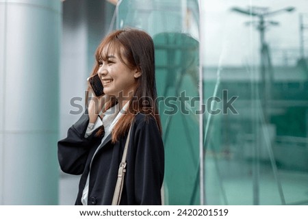 Young woman confident, attractive business happy smiling woman talking on mobile phone standing in city looking forward. Successful asian female work in business district