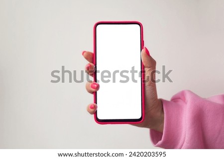 Close-up, no face, female hand in pink manicure sweatshirt pink nails holding smartphone in pink case with white blank screen for mockup or copy space on pastel gray background. Use of Applications