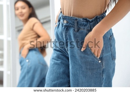 Young woman wearing trendy jeans near mirror in bedroom, closeup