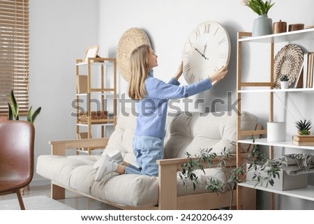 Young woman hanging big clock on wall at home Royalty-Free Stock Photo #2420206439