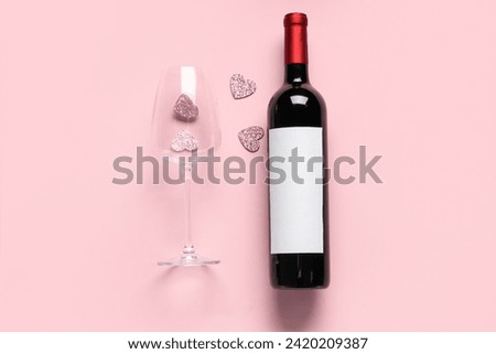 Bottle of wine with glass and hearts on pink background. Valentine's Day celebration
