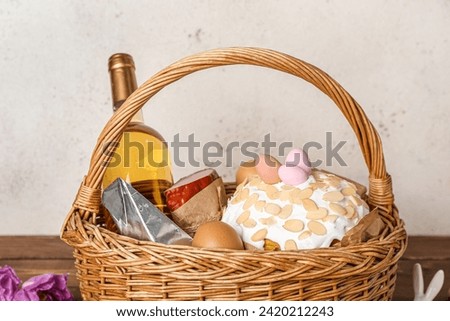 Basket with Easter eggs, cake and bottle of wine on wooden table against grey background