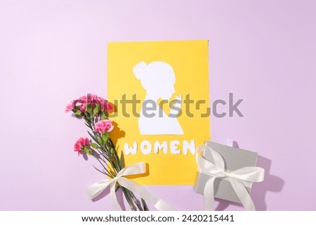 Yellow paper with a shape of a woman and the word “Women” made of paper featured. A small ring box displayed with a bouquet. International Women's Day celebrates the achievements of women worldwide