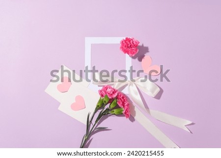 A white paper cut in a frame shaped arranged with pink flowers, paper hearts and a ribbon bow. Empty space inside the frame to display your photo or picture. Happy Women's Day concept