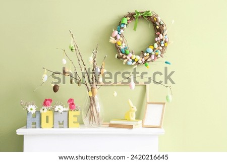 Mantelpiece with decor and Easter wreath on green wall in room Royalty-Free Stock Photo #2420216645