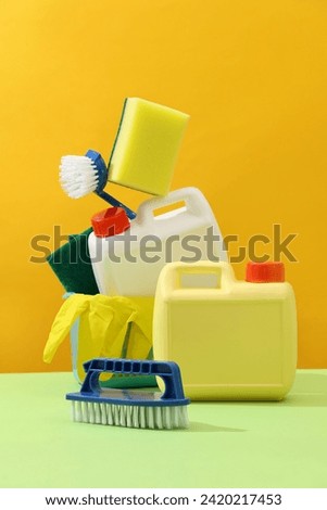 Creative idea for advertising detergents products. White and yellow plastic canisters with brushes, sponges and rubber gloves decorated on yellow background. Mockup blank label for design