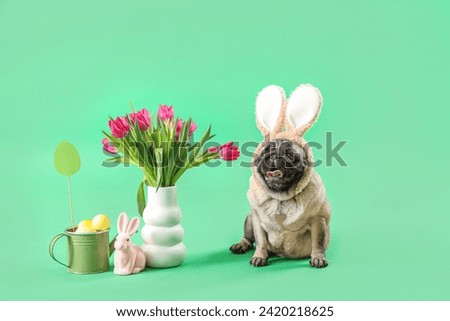 Cute pug dog in bunny ears with Easter rabbit, eggs and tulips on green background
