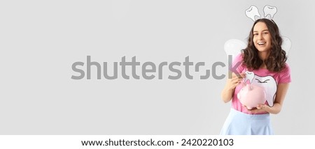 Tooth fairy with paper teeth and piggy bank on grey background with space for text