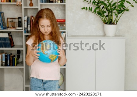 cute girl carefully examines the globe against the background of a bookshelf.