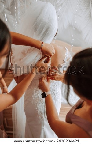 Wedding morning. Bridesmaids help put on the white wedding dress. A young woman is preparing to meet her groom and having fun with her friends Royalty-Free Stock Photo #2420234421