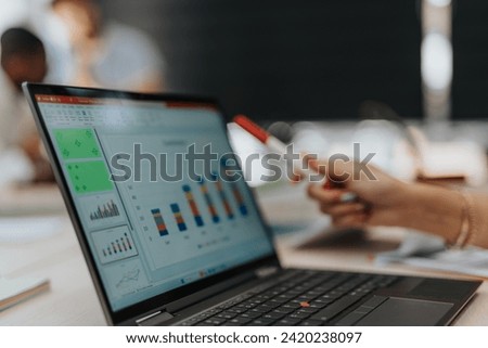 Close up shot of a lap top and a woman pointing with a marker to a graph charts. High quality photo.