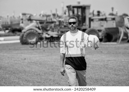 Mature architect walking in construction area. employee construction man in vest protective hardhat walking outdoor. Construction site with heavy machine and worker. caucasian construction manager