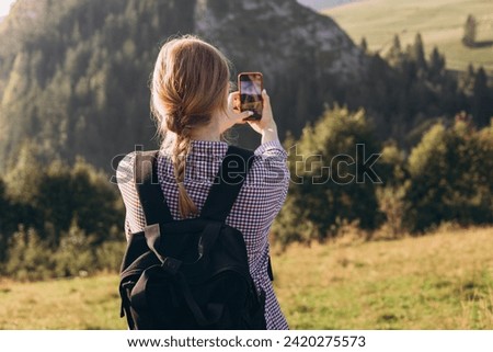 Tourist on top of the mountain takes a photo. Woman traveler takes a photo on a modern smartphone, makes beautiful pictures of beautiful mountain landscapes. Active lifestyle concept, rear view