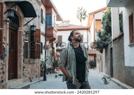 Portrait of a male tourist on a picturesque street of the old town.  A young, handsome guy in a light shirt walks through the green, narrow streets of the ancient city center Royalty-Free Stock Photo #2420281297