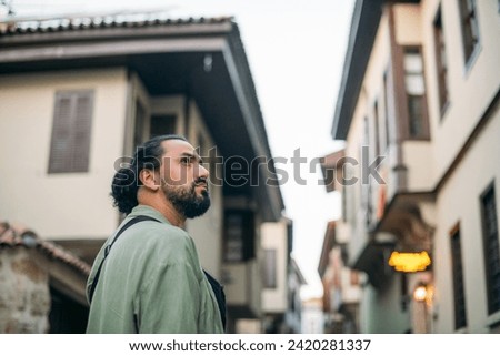 Portrait of a male tourist on a picturesque street of the old town.  A young, handsome guy in a light shirt walks through the green, narrow streets of the ancient city center Royalty-Free Stock Photo #2420281337