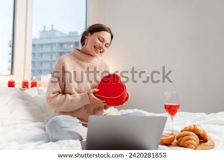 Beautiful smiling woman holding girt box using laptop having online dating. Distance relationship, love, Valentine's Day concept Royalty-Free Stock Photo #2420281853