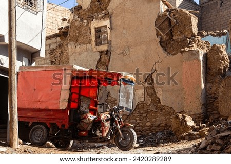 Amidst urban wreckage, a red trike stands resilient. Crumbling walls, scattered debris, and a clear sky tell the poignant tale of destruction and defiance Royalty-Free Stock Photo #2420289289
