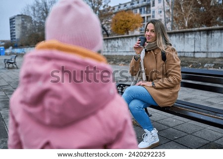 On a bench, the mother sips coffee, engaging in heartwarming conversation with her daughter—an intimate moment filled with warmth and connection.                           