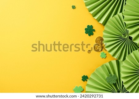 Cheerful clover celebration: St. Paddy's delight. Top view photo of paper folding fans, trefoils, coins on yellow background with space for festive text